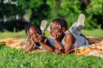 Two african girls lying on blanket in park smiling and having fun