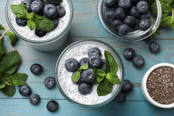 Delicious chia pudding with blueberries and mint in glasses on light blue wooden table, flat lay
