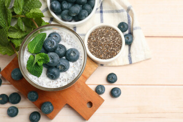Delicious chia pudding with blueberries and mint in glass on wooden table, flat lay. Space for text