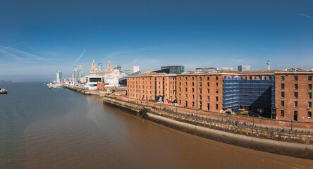 Aerial view of Liverpool showcasing the Royal Liver Building, Albert Dock, and the River Mersey. Historic and modern architecture are visible under clear skies.