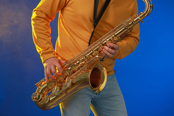 Naklejka premium Professional musician playing saxophone on blue background, closeup