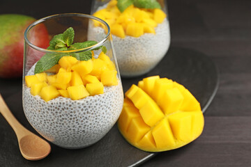 Delicious chia pudding with mango and mint in glasses on dark table, closeup