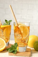 Refreshing iced tea with drinking straws, mint, lemon and lime on light textured table against grey background, closeup