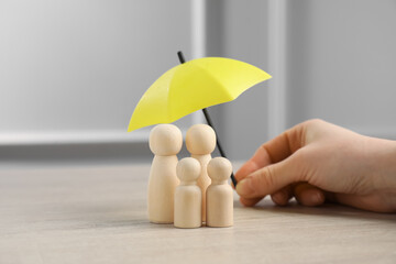 Woman holding umbrella over human figures at light wooden table, closeup. Insurance concept