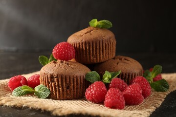 Delicious muffins with raspberries and mint on dark textured table, closeup