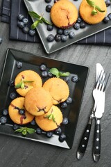 Delicious muffins with blueberries, mint and cutlery on dark textured table, flat lay