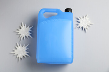 Antifreeze in plastic canister and decorative snowflakes on grey background, flat lay