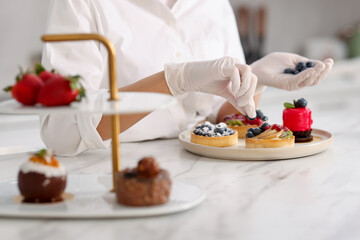 Confectioner decorating tart with blueberry at table, closeup