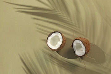 Fresh coconut and shadow cast by tropical palm on light green background, top view. Space for text