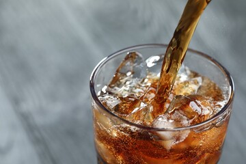 Pouring refreshing cola into glass on blurred grey background, closeup. Space for text