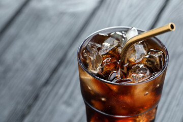 Refreshing cola with ice cubes and straw in glass on blurred grey background, closeup. Space for...