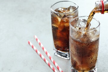 Pouring refreshing cola into glass on light table, closeup. Space for text