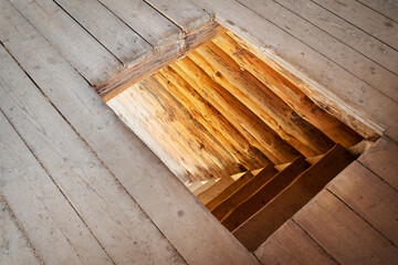 Old wooden flooring with a square hole revealing rustic log stairs leading downwards