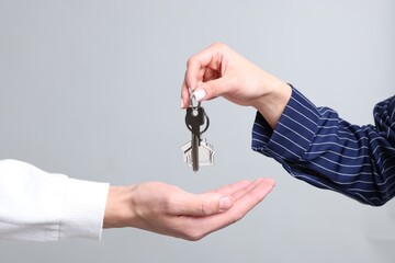Real estate agent giving house key to new owner on gray background, closeup