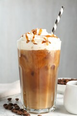 Tasty iced coffee with whipped cream, syrup and beans on white table