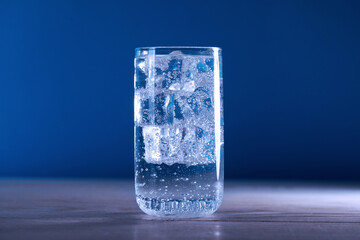 Refreshing soda water with ice cubes in glass on wooden table against blue background, closeup