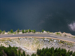 Aerial view of curved road alongside lush green forest and tranquil lake waters