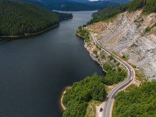Aerial view of curved road alongside lush green forest and tranquil lake waters