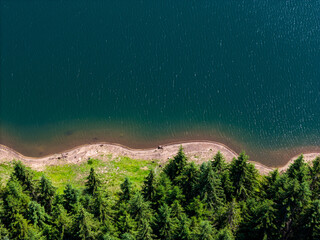 Aerial view of curved road alongside lush green forest and tranquil lake waters