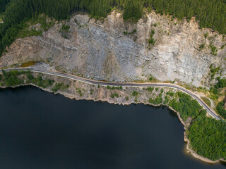 Aerial view of curved road alongside lush green forest and tranquil lake waters
