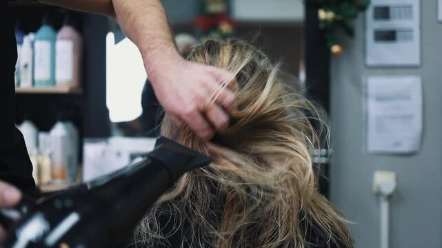 Professional hairdresser making a beautiful hairstyle to a beautiful woman after dyeing hair and making highlights in hair salon.