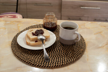 Freshly toasted bread spread with vibrant jam, steaming coffee mug, glass preserve jar resting on rustic kitchen counter, embodying morning's cozy warmth