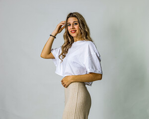 Smiling young woman in casual clothes sitting on stool on white background – relaxed and modern...