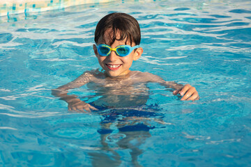 Child wearing swimming goggles swim in a pool on a sunny day.