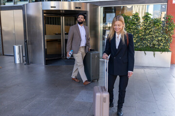 Two business travelers, a man and a woman, arrive at the entrance of a hotel, pulling their suitcases and ready to enjoy their stay, anticipating the services and hospitality that awaits them