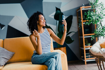 Young woman enjoying a relaxed moment at home, smiling and interacting on her phone while sitting...