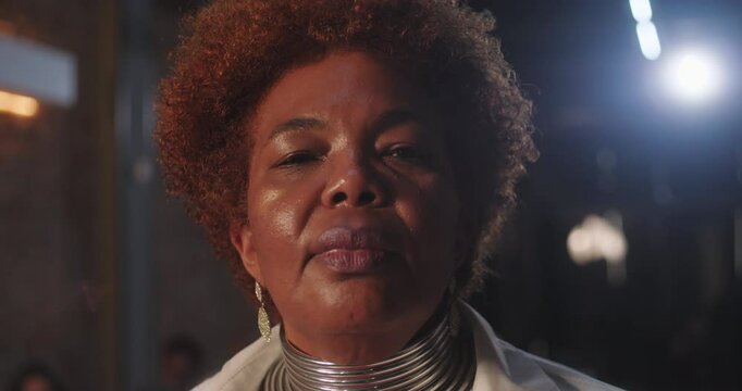 African American elderly woman with natural curly hair and statement necklace looking directly at the camera in a bold and assertive pose, indoor setting
