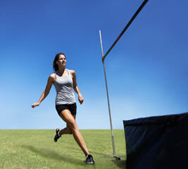 Woman, running and high jump athlete for sport training outdoor for competition, endurance or practice. Female person, leap and agility for cardio exercise or contest fitness, blue sky or flexible