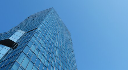 Modern glass building against a clear blue sky viewed from below.