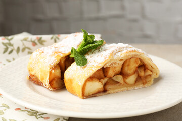 Pieces of tasty apple strudel with powdered sugar and mint on grey table, closeup