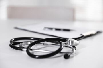 Stethoscope and paperwork on white desk in hospital, selective focus. Space for text