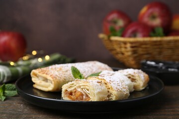 Tasty apple strudels with powdered sugar and mint on wooden table, closeup