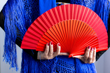 Female hands holding red fan with blue shawl in vibrant composition
