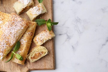 Tasty apple strudels with powdered sugar and mint on white marble table, top view. Space for text