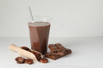 Tasty chocolate milk, bars and cocoa beans on white wooden table. Space for text