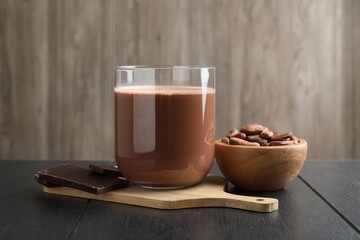 Tasty chocolate milk, bars and cocoa beans on black wooden table