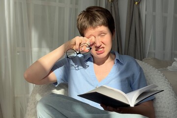 woman rubbing her eyes while reading a book