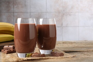 Tasty chocolate milk in glasses, pieces and bananas on wooden table, closeup. Space for text