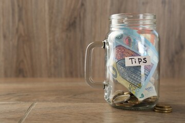 Mason jar with tips on wooden table, closeup. Space for text