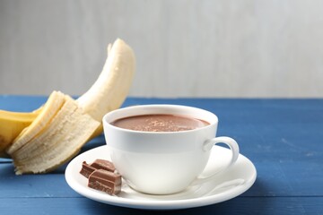 Tasty chocolate milk in cup, pieces and banana on blue wooden table, closeup