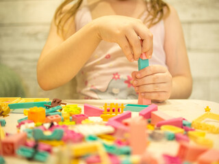 A young teenage girl assembles a construction set from plastic parts and blocks with her hands.