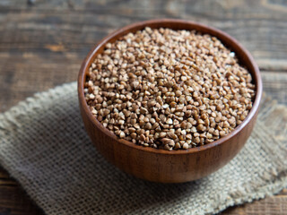Organic buckwheat groats in a wooden bowl with a spoon on a linen napkin on a wooden table.
