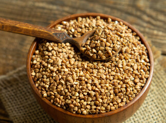 Organic buckwheat groats in a wooden bowl with a spoon on a linen napkin on a wooden table.
