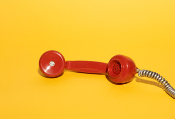 Vintage red phone handset on vibrant yellow background. A minimalistic retro composition with bold colors, evoking nostalgia and classic communication themes. Perfect for pop design concepts.