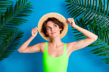 Young woman in vibrant summer outfit poses joyfully with straw hat against a blue tropical background