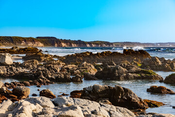 Waves crashing behind the rocky areas of the beaches in the town of Maitencillo, with cliffs in the background, Chile